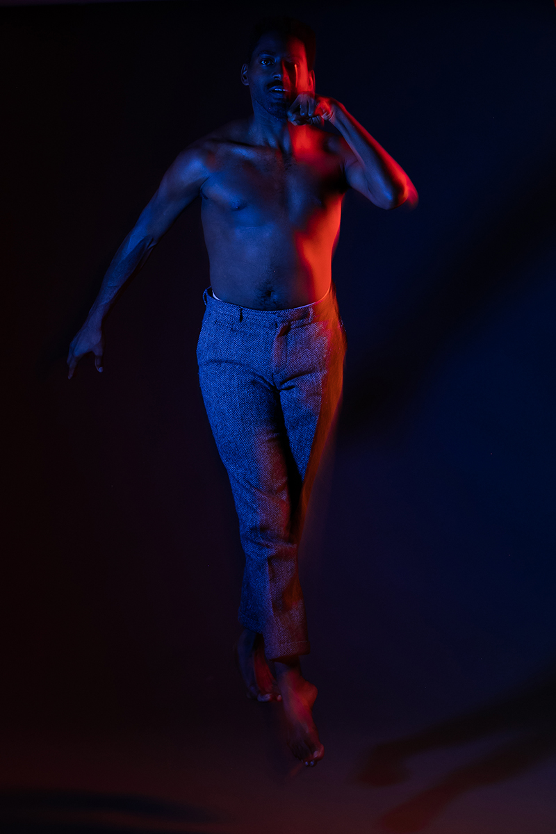 Color photo of Jerron leaping mid air in blue and red light, his left arm high near his face