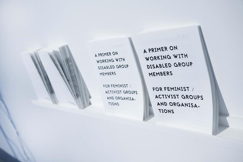 Multiple copies of a risograph pamphlet line a gallery wall.Romily Alice Walden's work 'A Primer on Working With Disabled Group Members for Feminist / Activist Groups and Organisations', 2018. 12 page, A4 risograph publication. Launched at AIR Gallery, NYC. Exhibited in the UK, USA, Germany and Poland. This document was produced in 2018 in response to experiences working with feminist and activist groups that were unprepared for working with disabled group members. The primer is an example of publishing as artistic practice; it positions information and education as a tool for change-making that can be embraced within a socially-engaged fine-art practice.