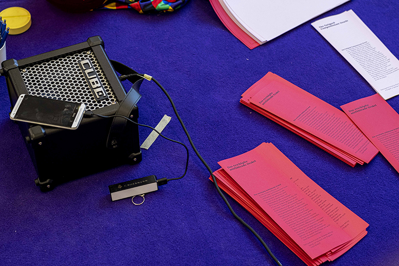 A stack of red pamphlets for the Oracle sit on deep purple carpet. Part of the project 'The Fatigued Compassionate Oracle' by Sickness Affinity group at Berlin Biennale 11