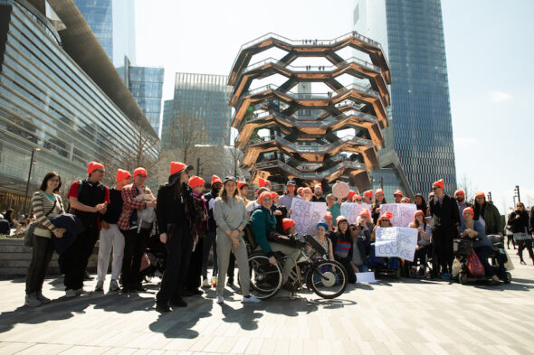 About 40 people posed in front of the Vessel sporting neon orange, Anti-Stairs Club Lounge beanies and holding Anti-Stairs Club Lounge Signs.