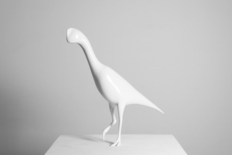 a white sculpture of a bird or dinosaur-like figure stands on a pedestal against a white wall