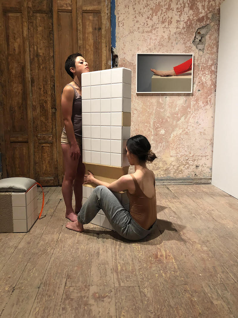 two women, one sitting, one standing, hold a tiled wall piece together