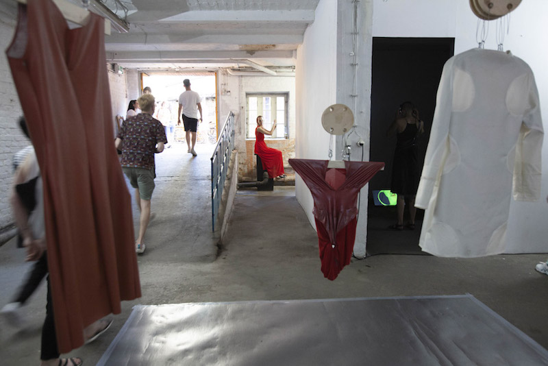 an art installation of hanging textiles in red and white tones shown in a gallery space