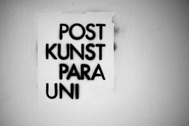 black graffiti writing on a white wall reading Post Kunst Para Uni