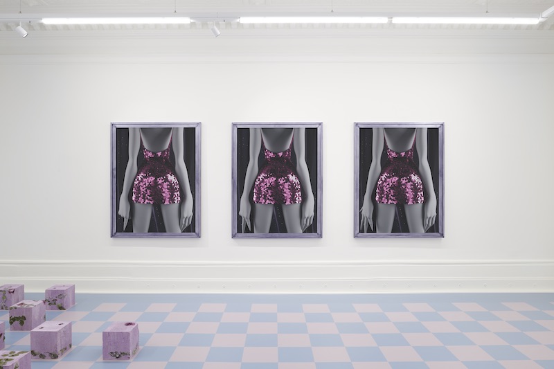 three identical portraits of a woman in a sequined dress are mounted on a gallery wall, with a checkered floor in the foreground and some undefined mauve box sculptures on the floor