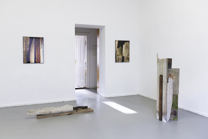 A view of the exhibition featuring two sculptures and two photographs in a white room.