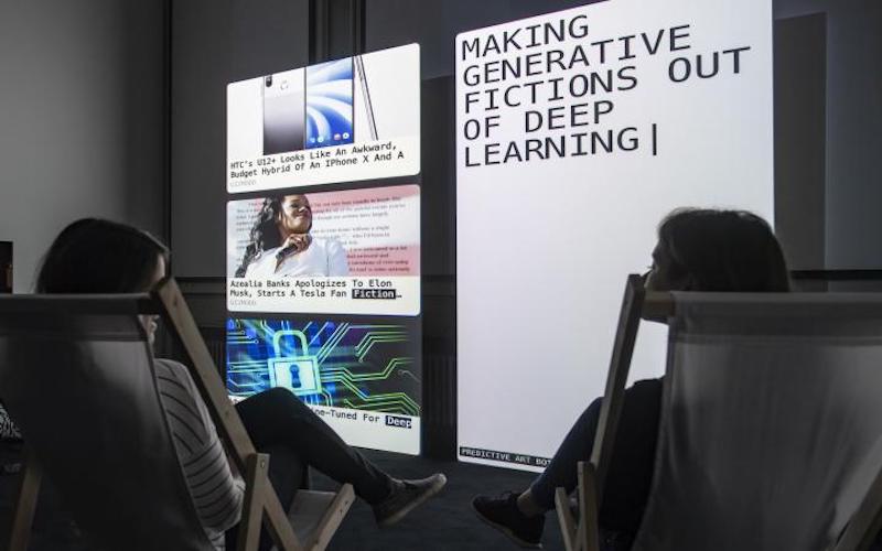 A photo of two people looking at computer screens reading "making generative fictions out of deep learning".