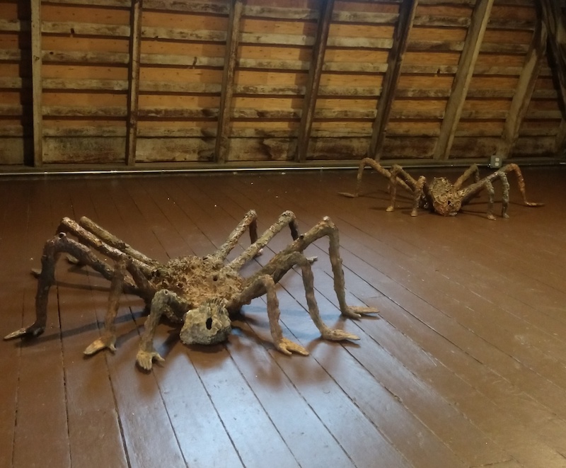 two large scale ceramic spiders positioned on a wooden attic floor