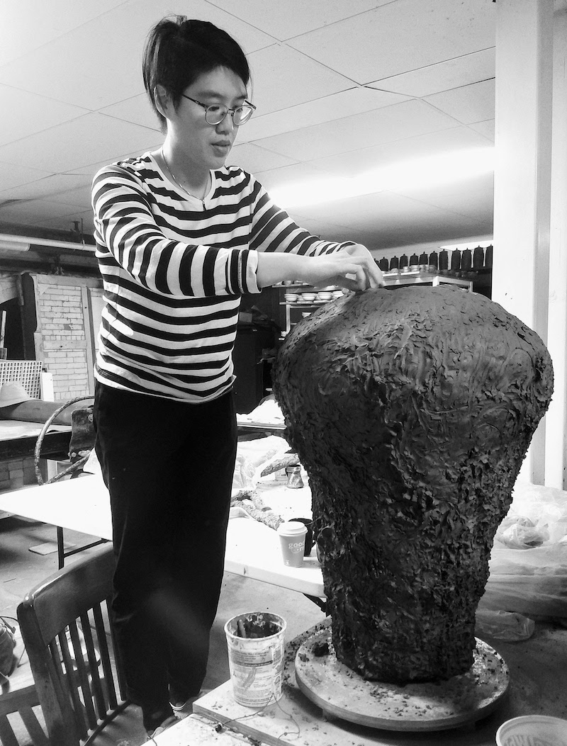 a black and white photo of the artist Heidi Lau shaping clay in her studio