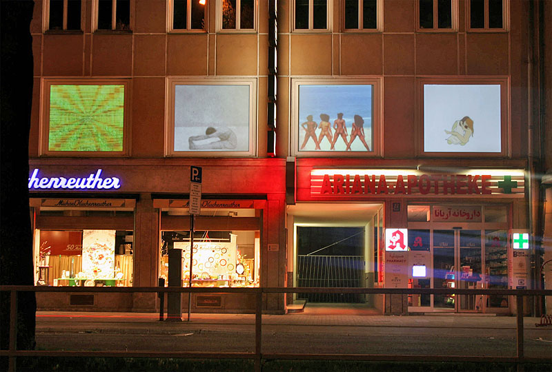 storefronts on a shopping street show video projections in their windows at night