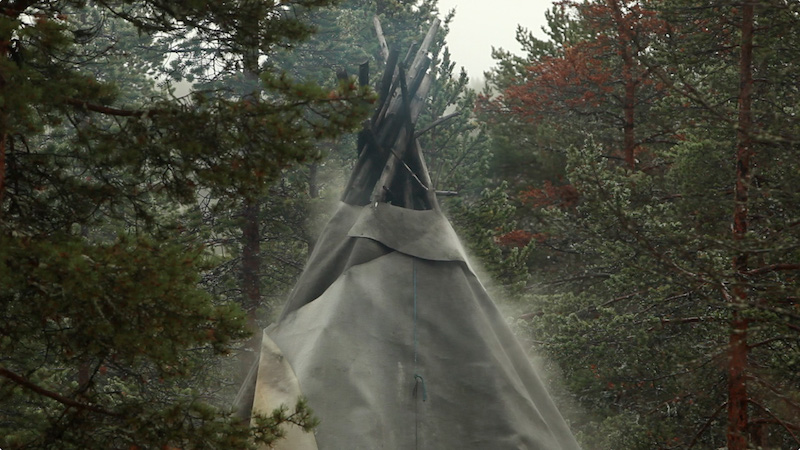 a video still of a Sami lavuu (tent) in a forest with mist rising up beside it