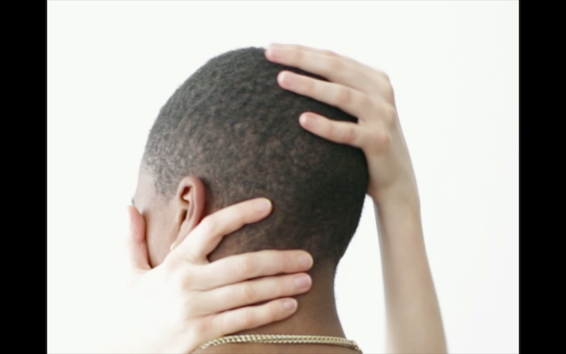 the back of a person's shaved head is caressed by two hands