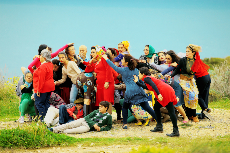 a group of people, some dressed in bright red, pose for a staged photo that looks as if in motion on a patch of grass