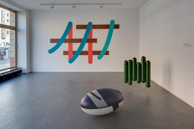 an installation view of the gallery's ground floor room with two colorful sculptures on the floor and a mounted abstract sign system
