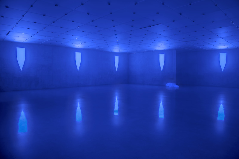 A blue lighted exhibition space at Kunsthaus Bregens showing blue lights reflected onto the concrete walls