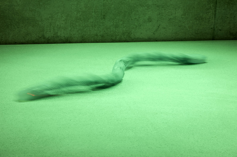 A robotic snake moving through the green lighted exhibition space of Kunsthaus Bregenz