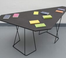 an angular black table with colorful Surhkamp books on top of it