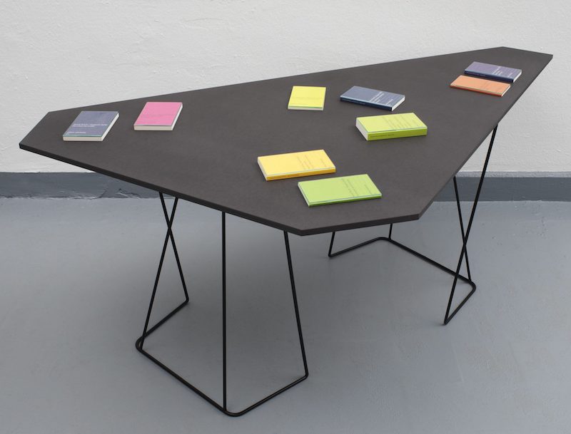 an angular black table with colorful Surhkamp books on top of it