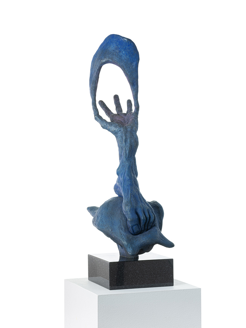 A surreal blue bronze sculpture of a hand that gives way directly to a foot. It looks like the foot is atop a turtle shell, or rounded figure of some kind. The thumb and pinky fingers support a kind of parachute.