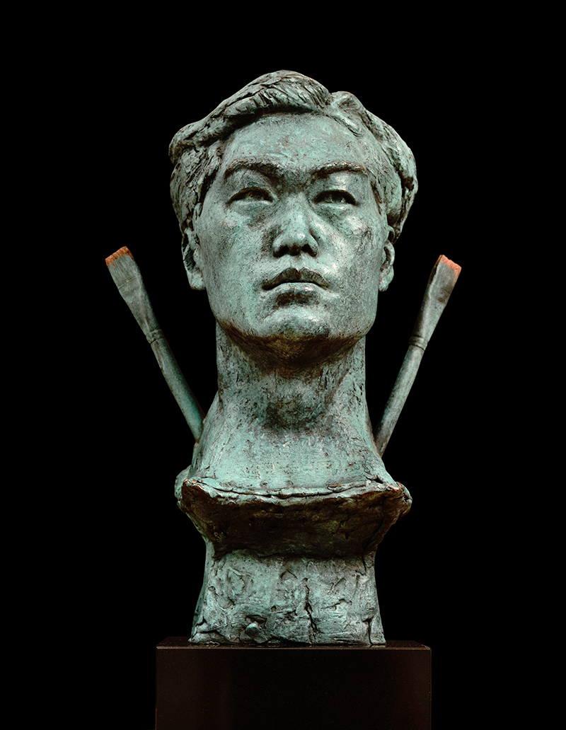 A bronze sculpture of a male head with two bronze paint brushes emerging from his neck