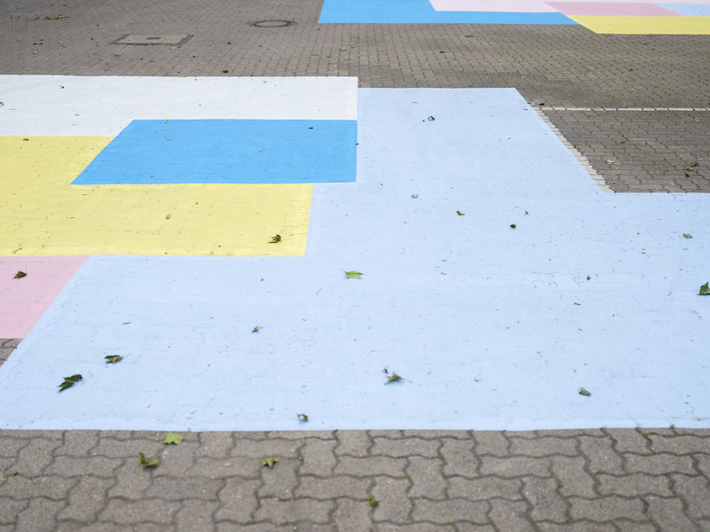 A close up of the blue, yellow, white and pink colored square shapes painted on a courtyard ground