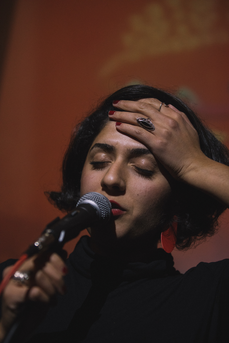 a close up of the poet speaking into a microphone while one hand is pressed against her forehead