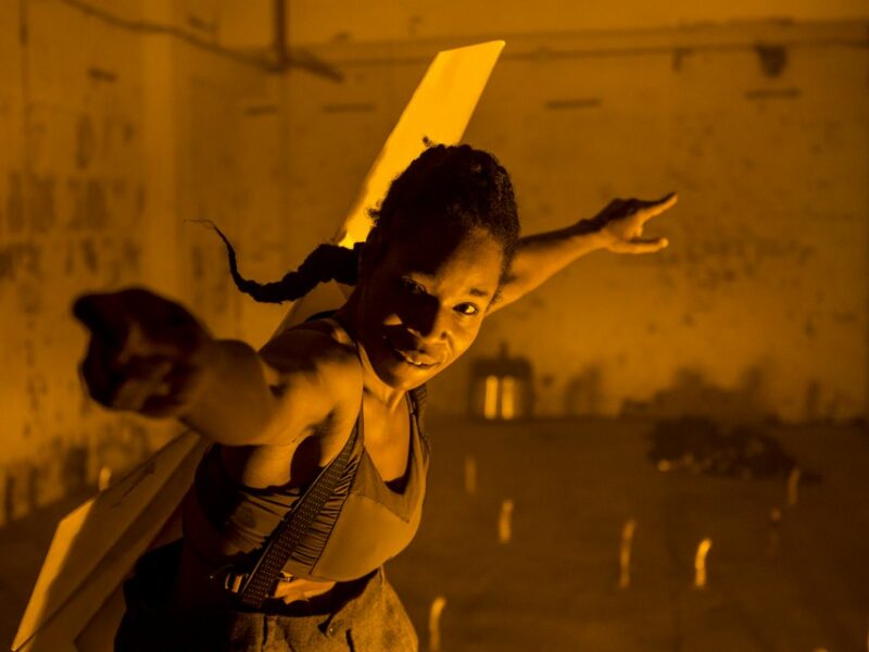 A woman spreading her arms during a performance in a room with orange lighting