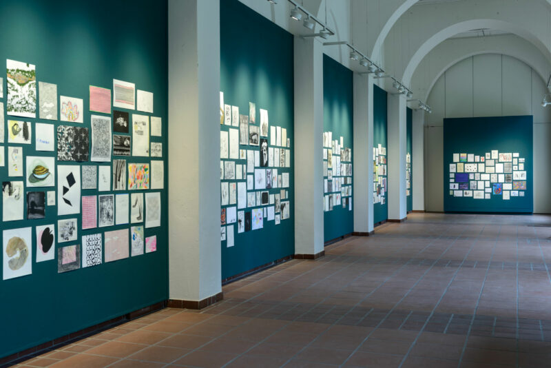 Exhibitiion room with green walls and many drawings placed on them