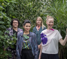 a group of four women who are part of the Estonian Pavilion artistic team posing in front of some green foliage