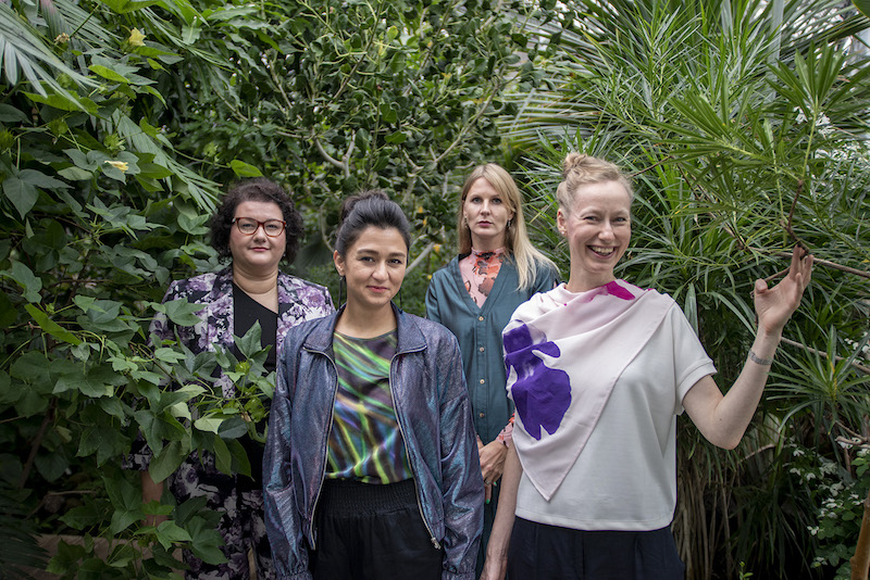 a group of four women who are part of the Estonian Pavilion artistic team posing in front of some green foliage