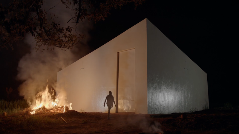 a fire burning next to the White Cube museum building and a figure walks along the side of the wall