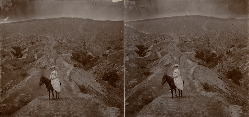 a grainy black and white archival photograph of a woman in a white dress riding a black horse in an arid mountainous setting