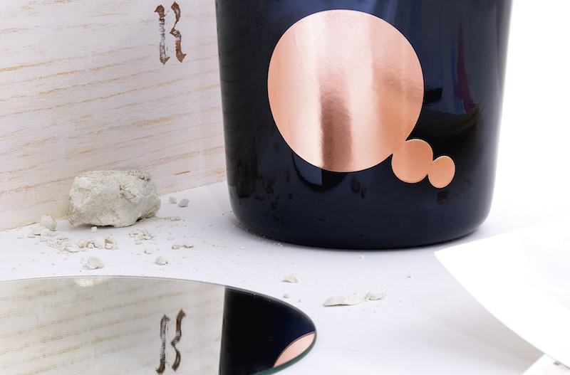 a close up detail of the champagne bottle with the artist's rose pink bubble label and a piece of chalk next to it