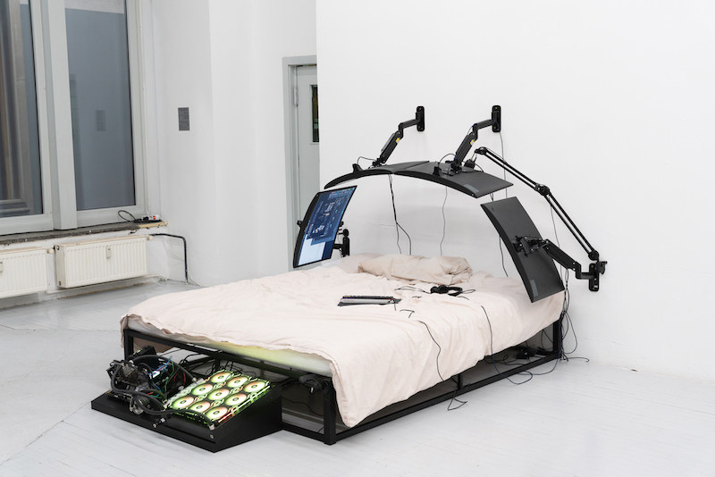 image of an installation artwork of a bed with computer monitors