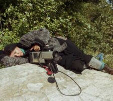 the filmmaker lies on a large rock, sleeping next to her camera