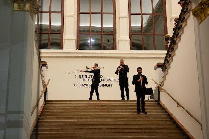 an ensemble of musicians play their instruments on the stairwell of Gropius Bau