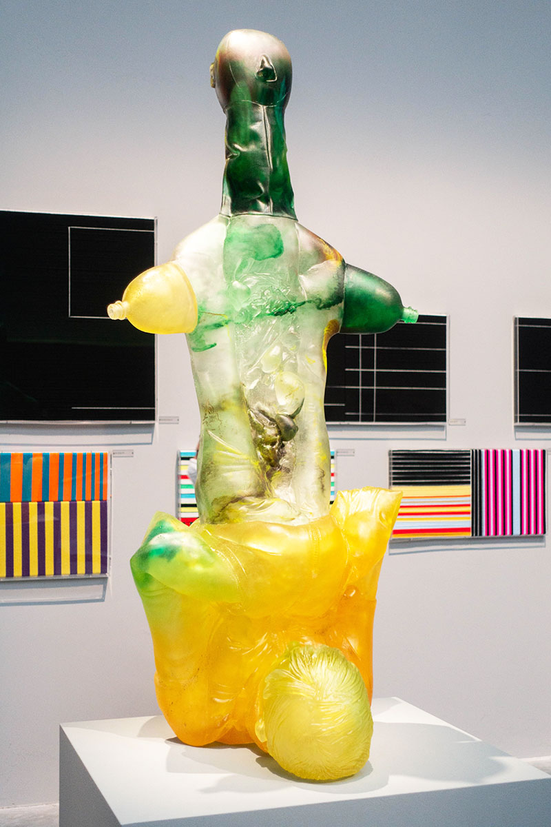 A sculpture made of glass in yellow and green showing a kind of amputated body with plastic bottle arms