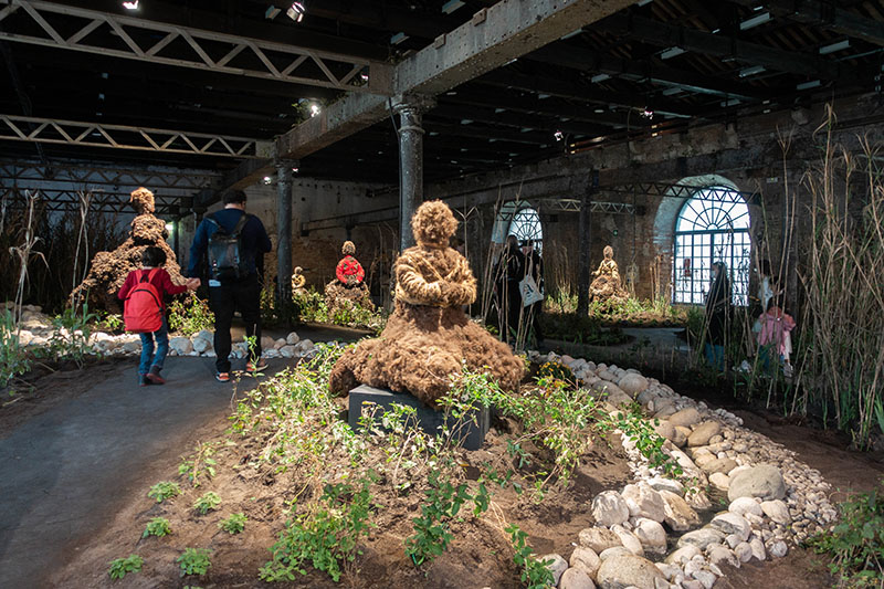 People walking through an garden created by artist Precious Okoyomon showing a sculpture made of earth 