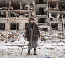 Well dressed older woman in a fur coat standing in front of bombed out apartment