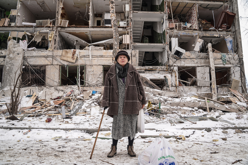 Well dressed older woman in a fur coat standing in front of bombed out apartment