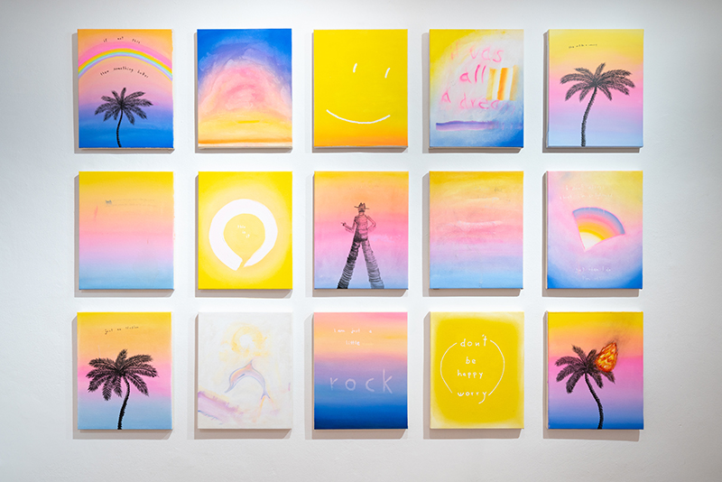 a wall with 15 small paintings in blue pink and yellow hung in a grid