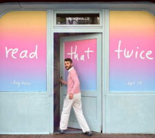 A man in white trousers and pink pullover walking into a shop whose windows have been covered with adhesive vinyl with the words "read that twice" on it