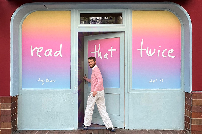 A man in white trousers and pink pullover walking into a shop whose windows have been covered with adhesive vinyl with the words "read that twice" on it