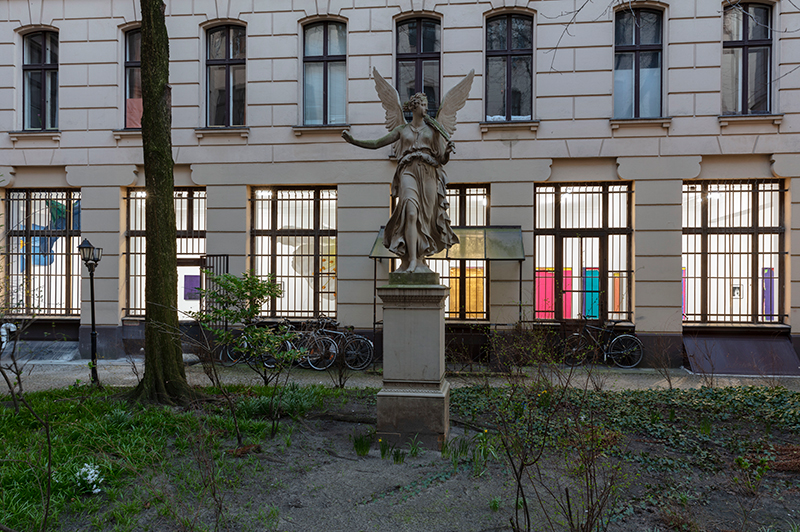 Statue of an angel on a plinth in front of a building with an art gallery inside
