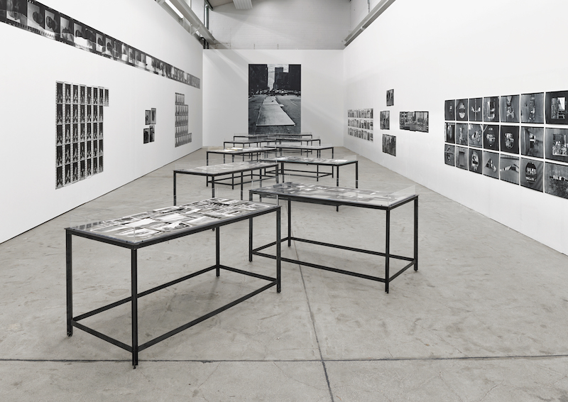 Photo of a large hall filled with black and white photographs. Many vitrines line the centre of the room