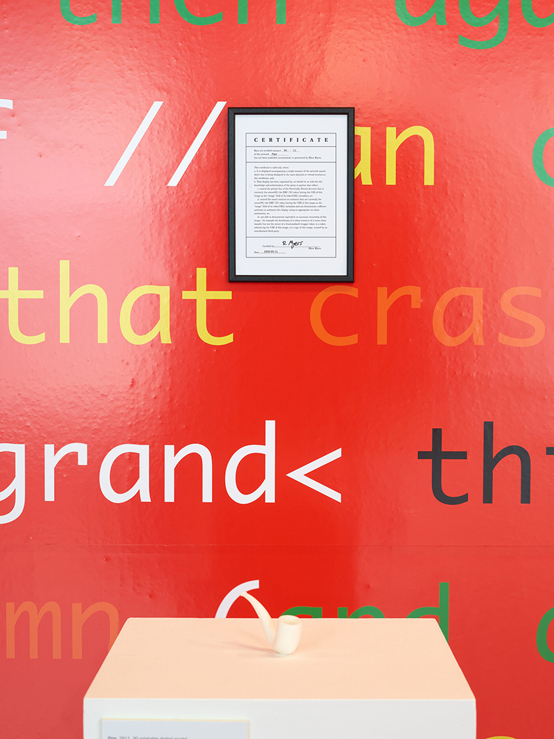 a framed certificate hanging on a red wall with words printed on it and a plinth with a white pipe in the foreground