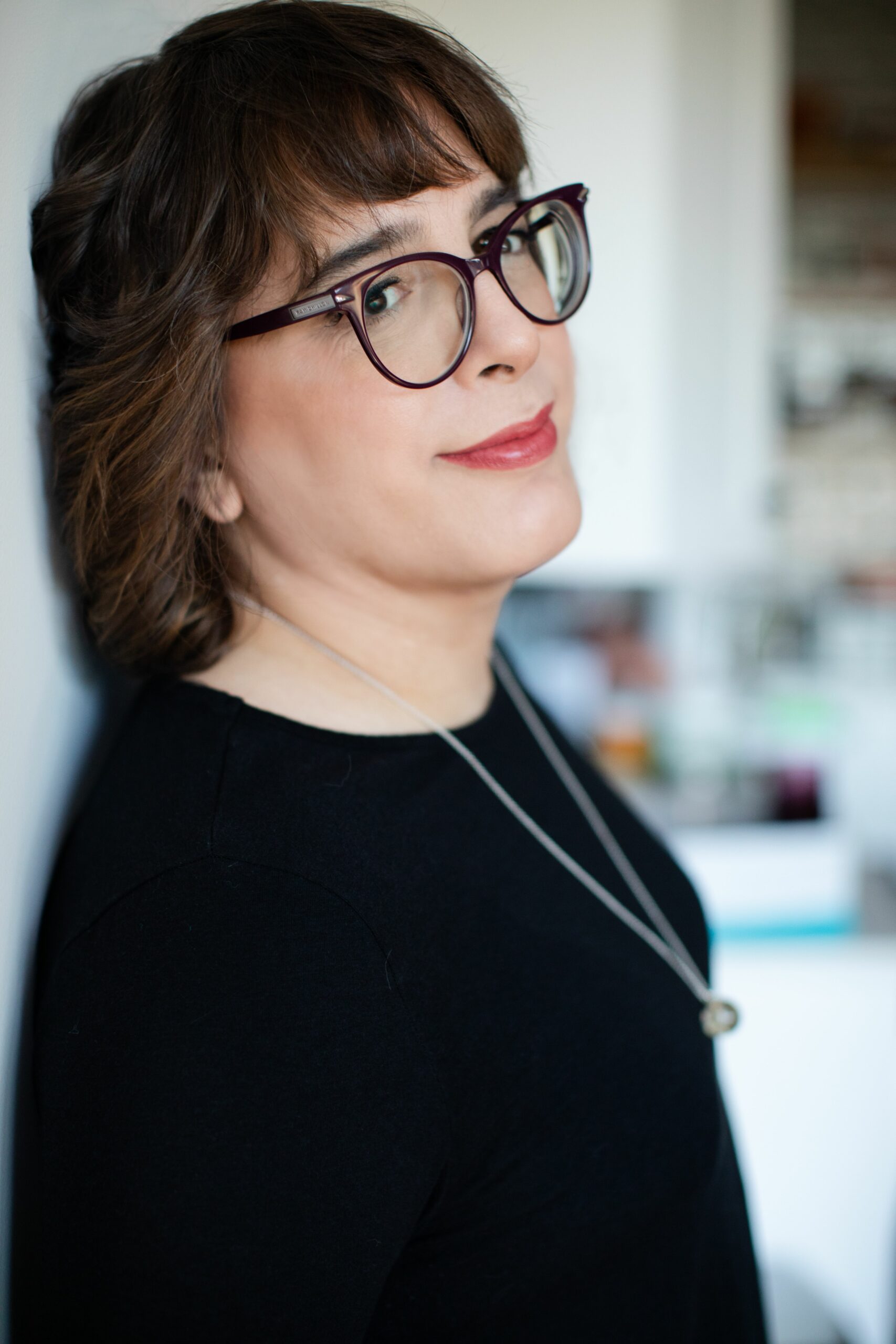 a portrait photograph of a woman leaning against a wall and looking into the camera smiling