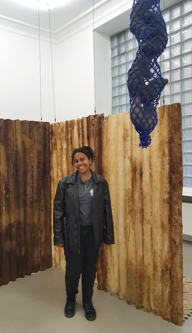 Sofia Rosales is standing in front of her artwork in a gallery and smiling