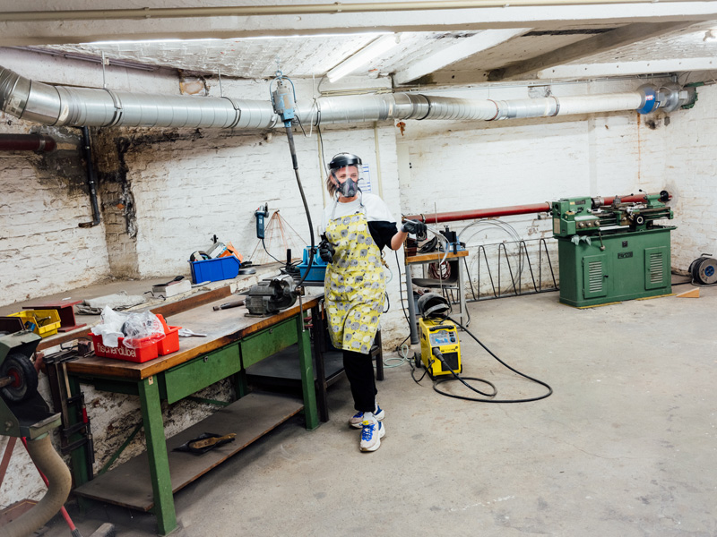 Artist Vanessa Brown wearing in her workshop, wearing an apron and metal cutting gear