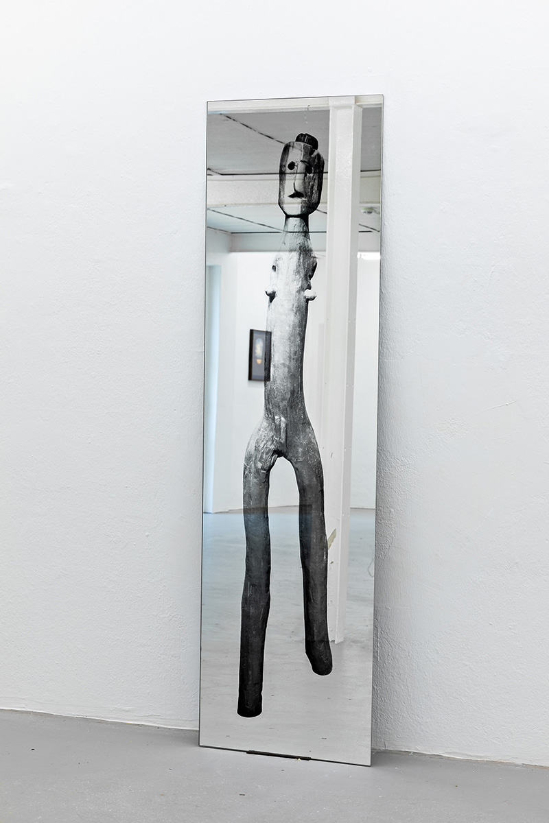 A floor length mirror leaning against the wall with a wooden human-like figure printed on it
